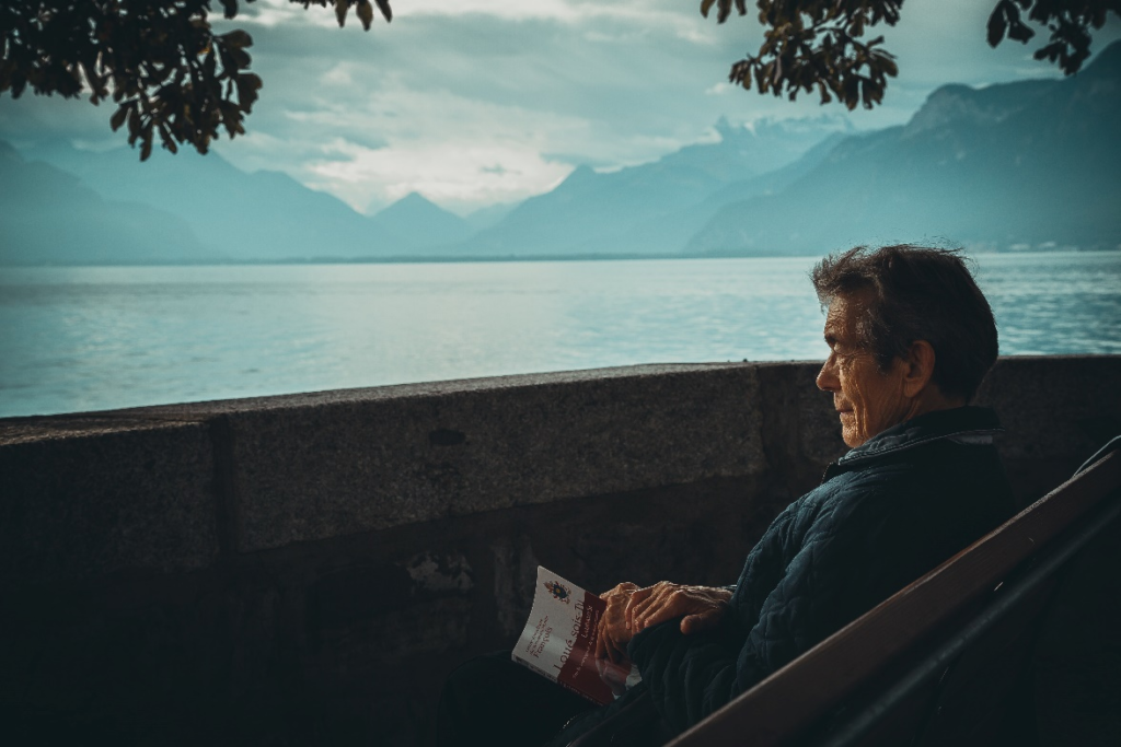 An elderly person sitting on a bench with a book