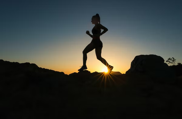 a woman running on a rocky terrain with the sun setting behind her