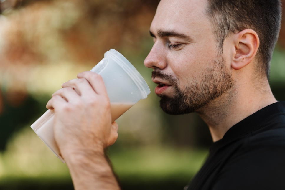Man holding a white plastic container with a protein shake